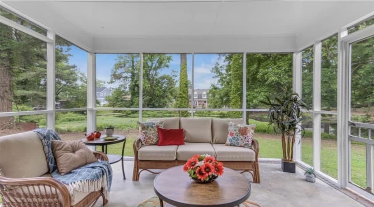 Screened porch with wicker furniture and view.