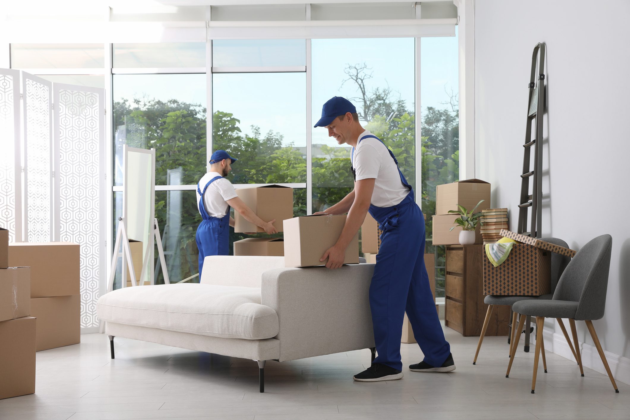 Movers carrying boxes in a bright room.